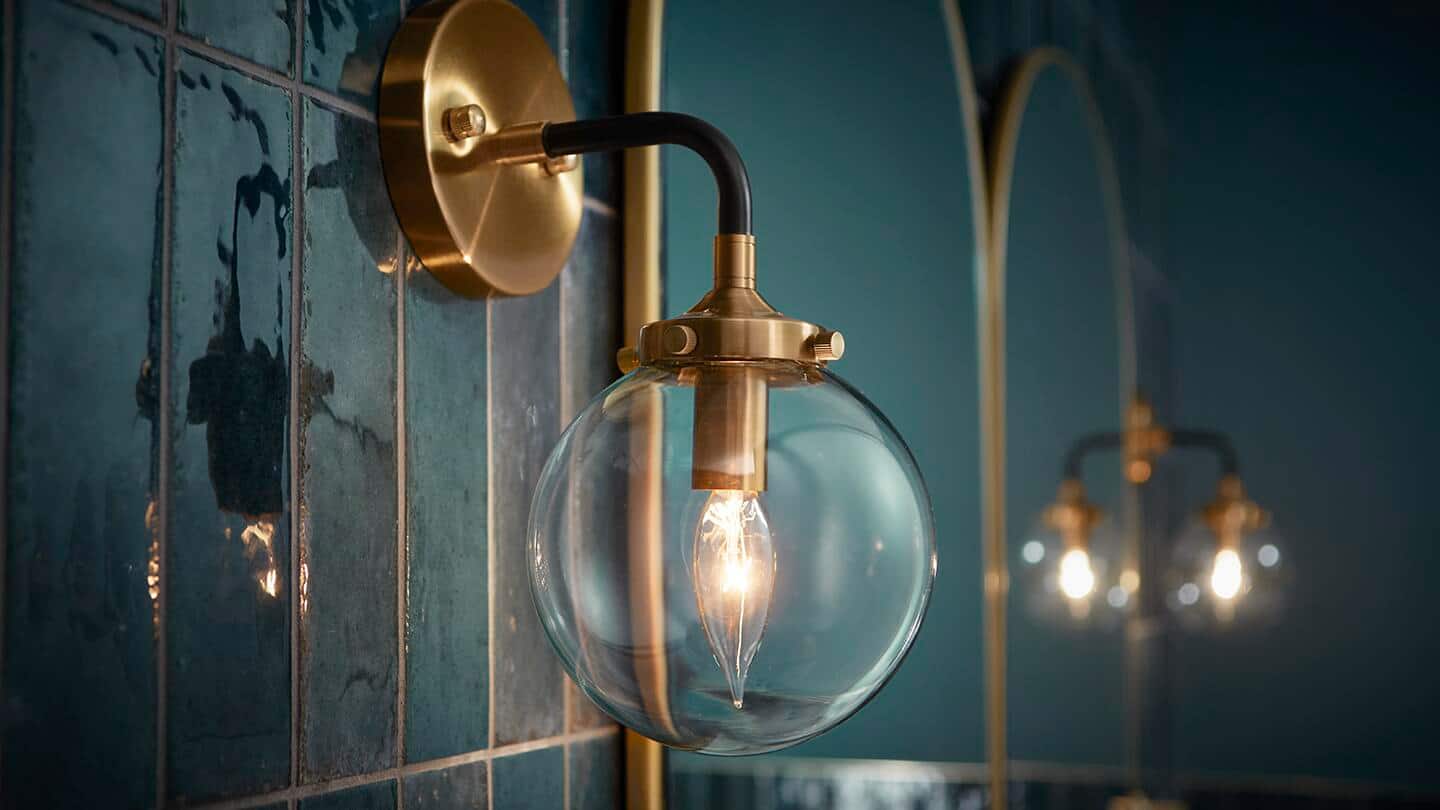 A wall sconce with a clear glass globe and a candle bulb hangs next to a bathroom mirror. A wall sconce with a clear glass globe and a candle bulb hangs next to a bathroom mirror.