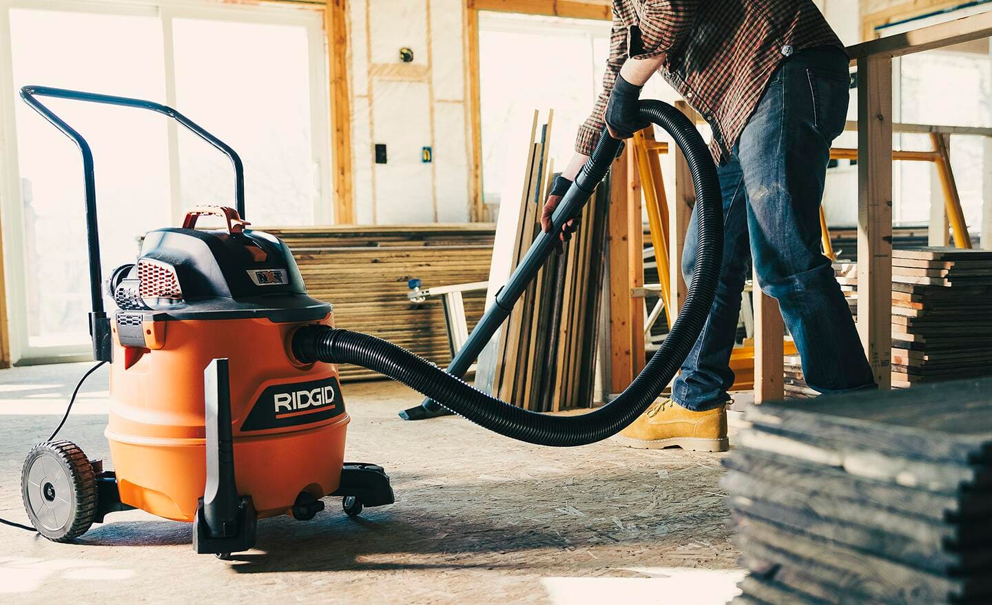 A person uses a shop vacuum to clean a subfloor.