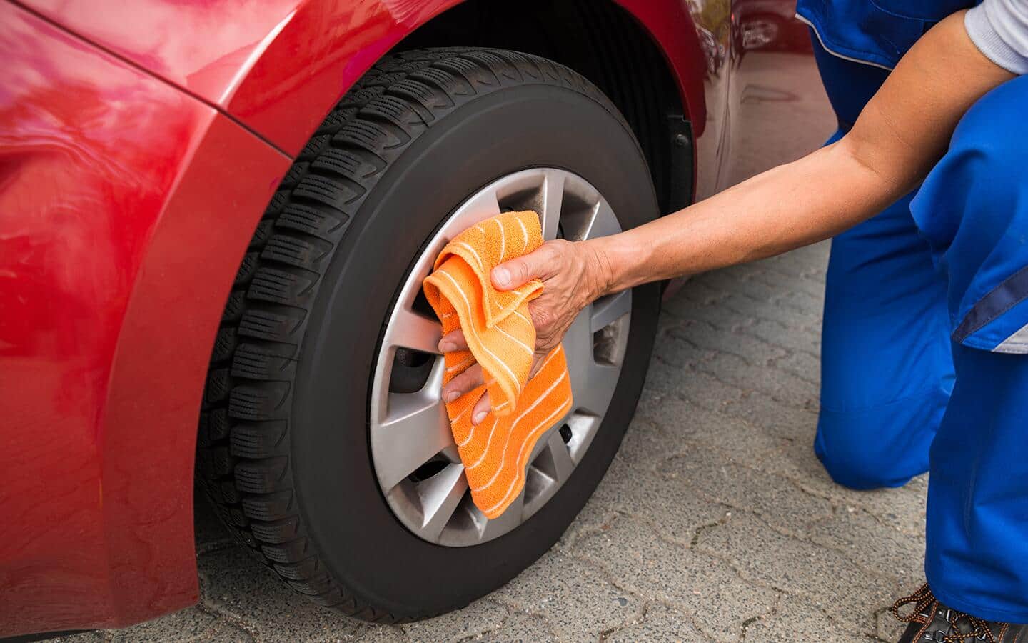 A person uses a small towel to dry a car wheel.
