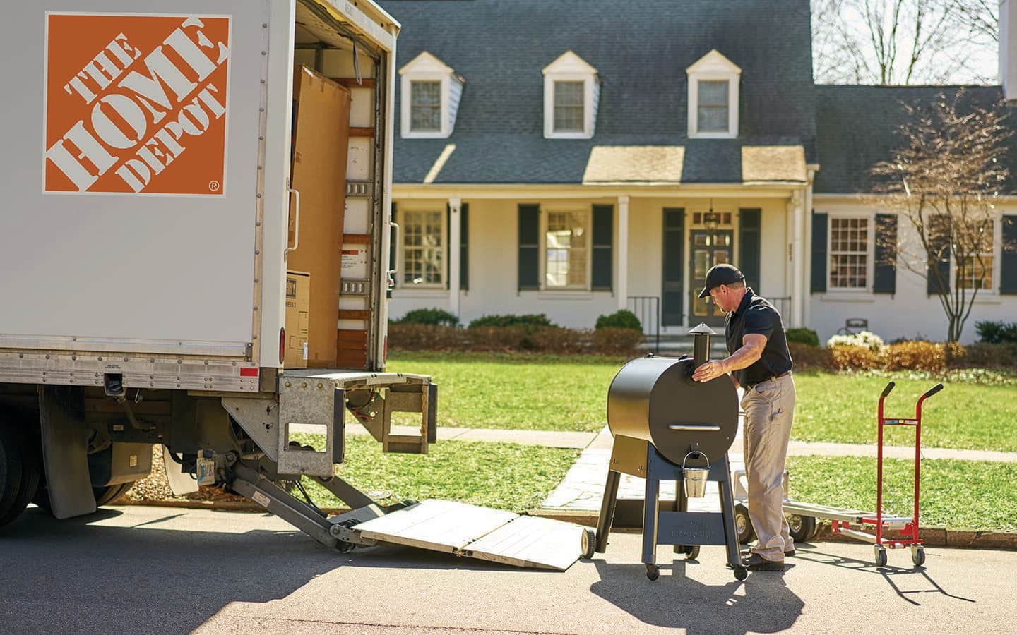 A Home Depot associate unloading a smoker in front of a house.