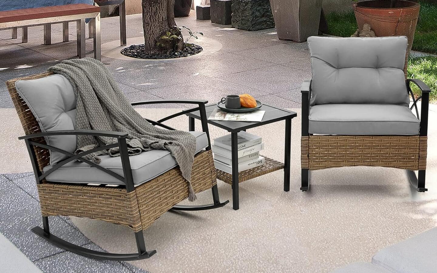 Two wood rocking chairs with gray cushions surrounding a side table on a neutral outdoor patio rug.