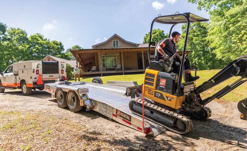 A Pro drives a mini-excavator off a trailer. A Pro drives a mini-excavator off a trailer.