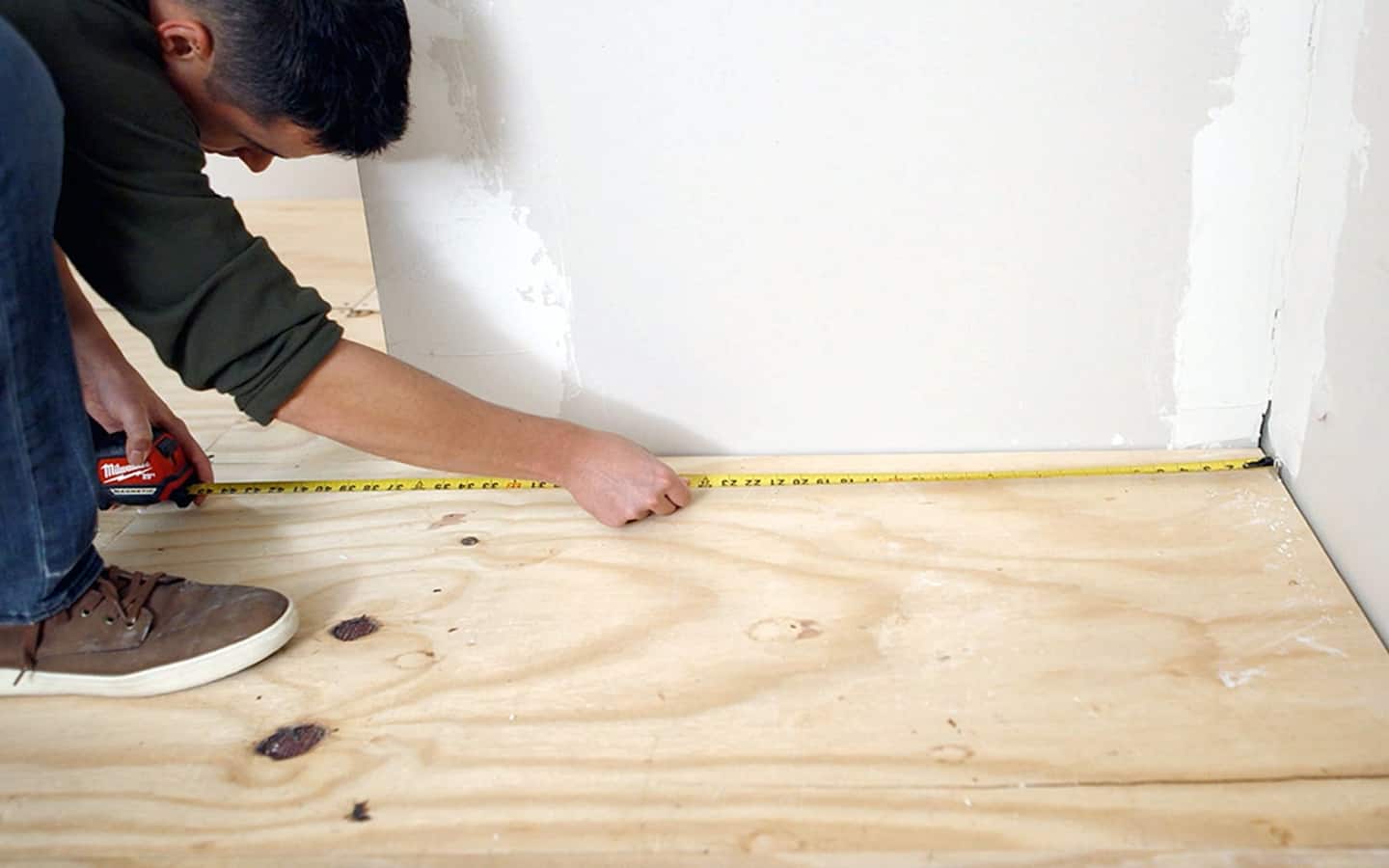 A Pro measures a wood subfloor with measuring tape.