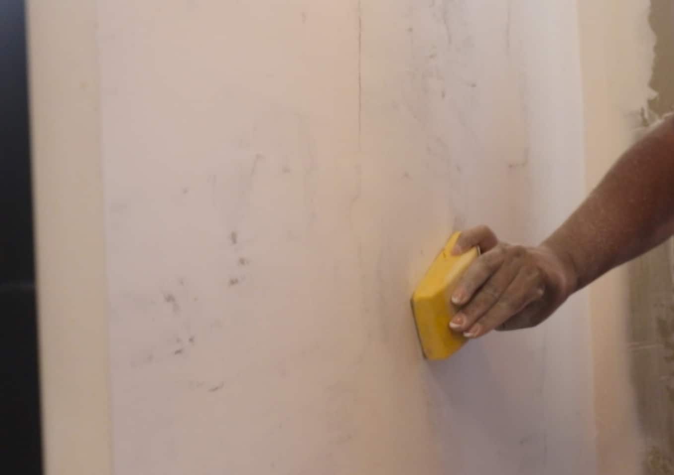 A person sanding a wall.