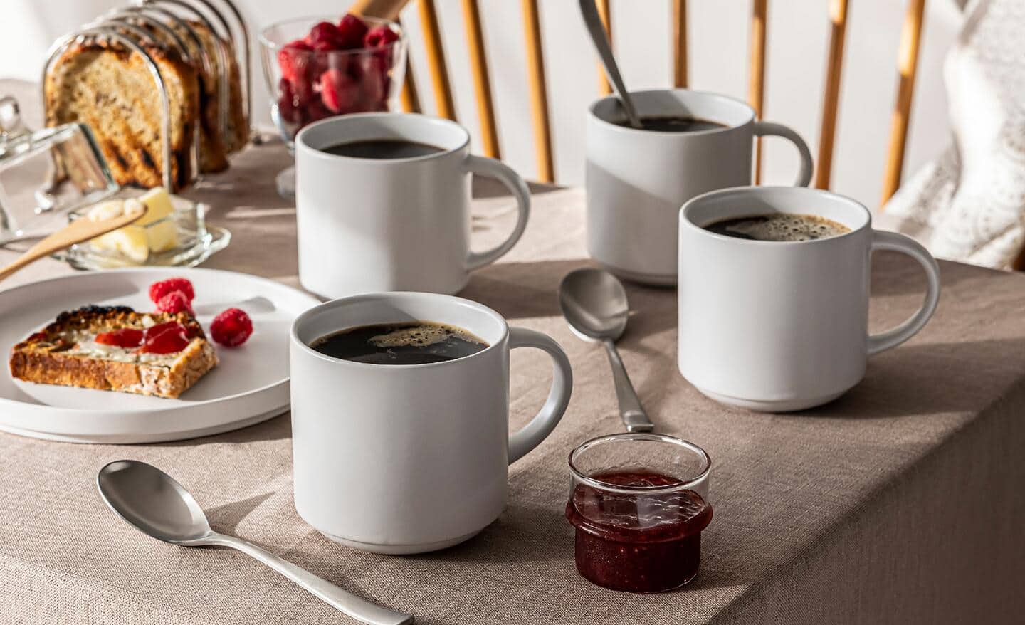 Four stoneware mugs with coffee sit on a table prepared for breakfast. Four stoneware mugs with coffee sit on a table prepared for breakfast.