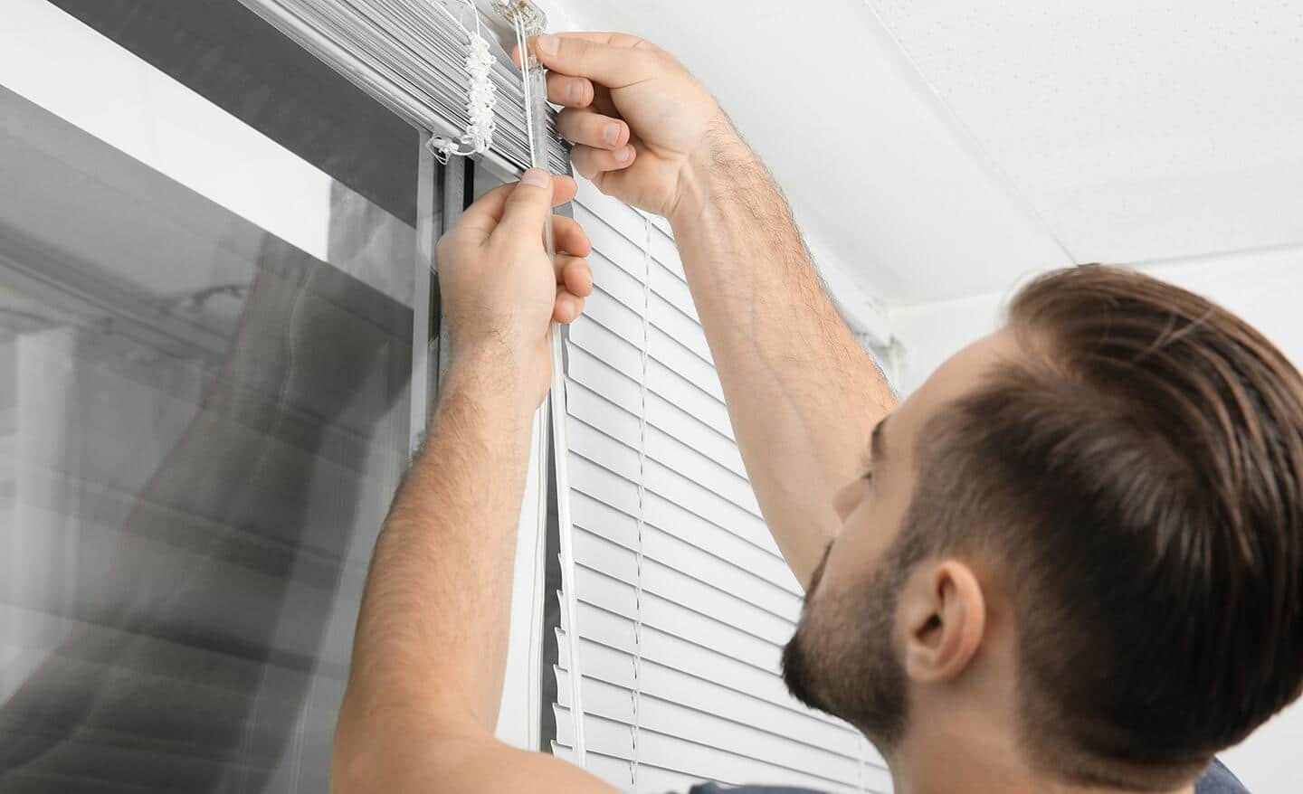 Man adjusting cordless blinds to ensure safety measures. Man adjusting cordless blinds to ensure safety measures.