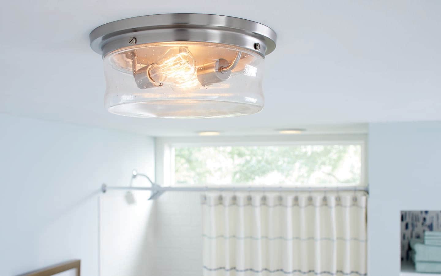 A flush mount lighting fixture hangs on a bathroom ceiling. A flush mount lighting fixture hangs on a bathroom ceiling.