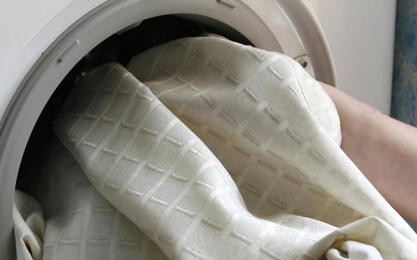 Curtains being placed in a washing machine.  Curtains being placed in a washing machine.