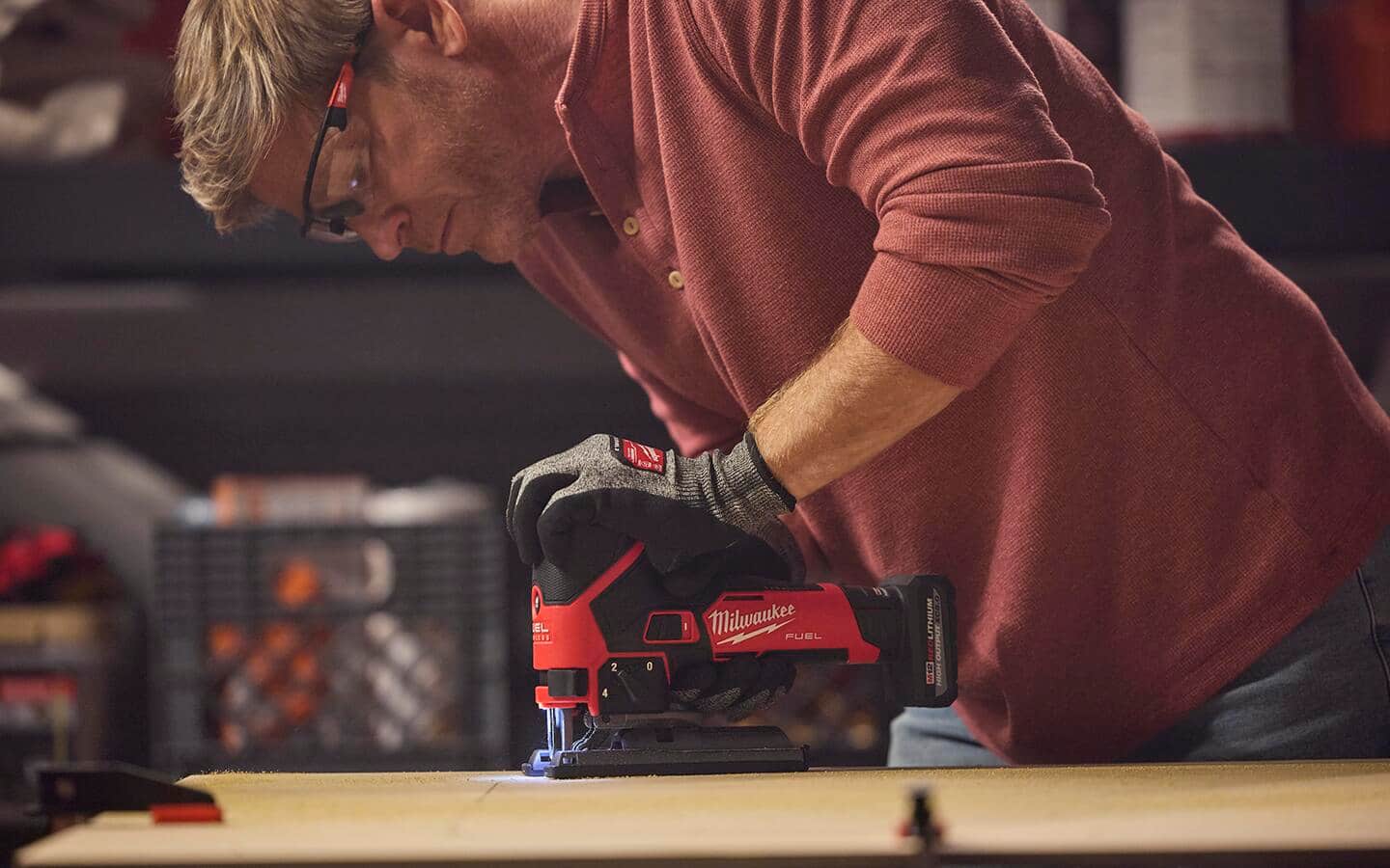 A person with safety glasses and gloves cutting a board with a jigsaw.