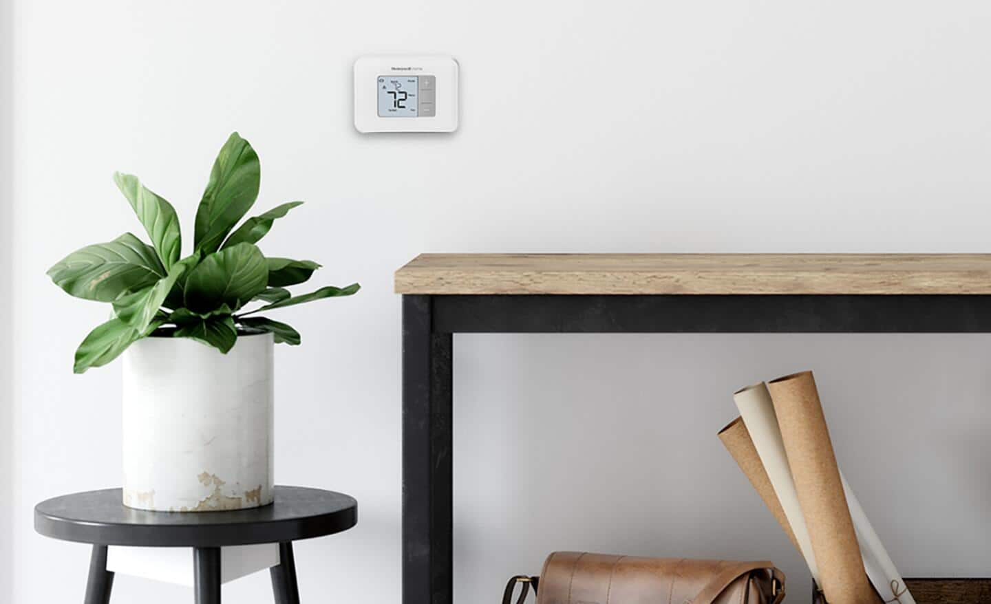 A manual thermostat on a white wall with a plant and a table in the foreground. 