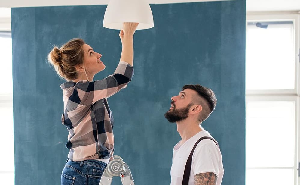 Two people change a light bulb in a ceiling fixture. 