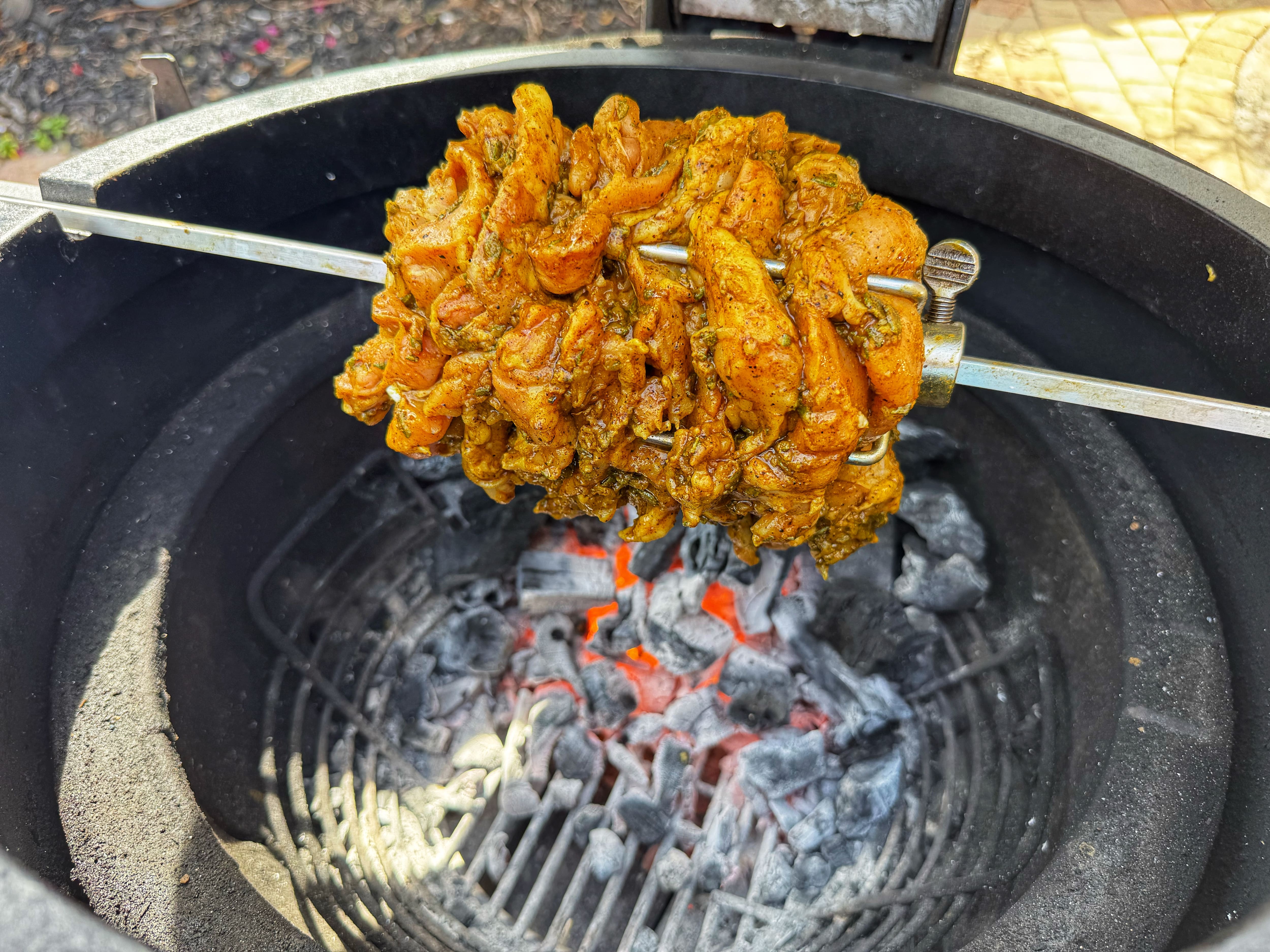 Raw seasoned chicken on a spit over a grill.