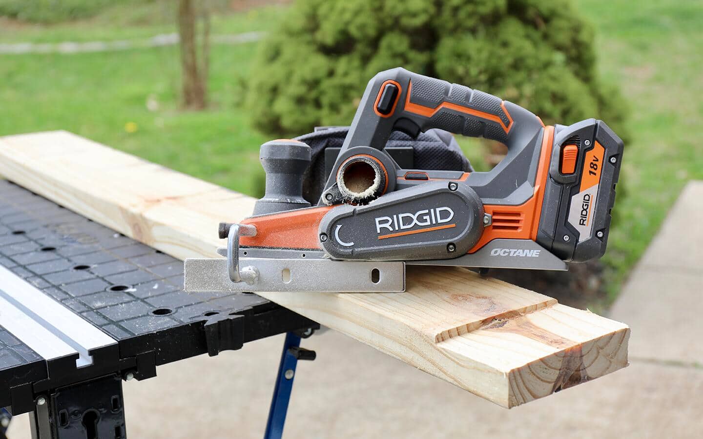 A hand planer, with an attached dust bag, sits on top of a piece of wood. A hand planer, with an attached dust bag, sits on top of a piece of wood.