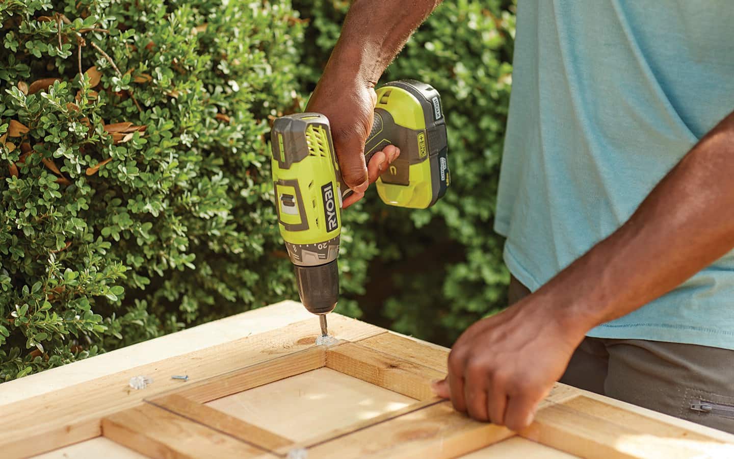 A person uses a drill to attach screws to the corner of a cold frame. 