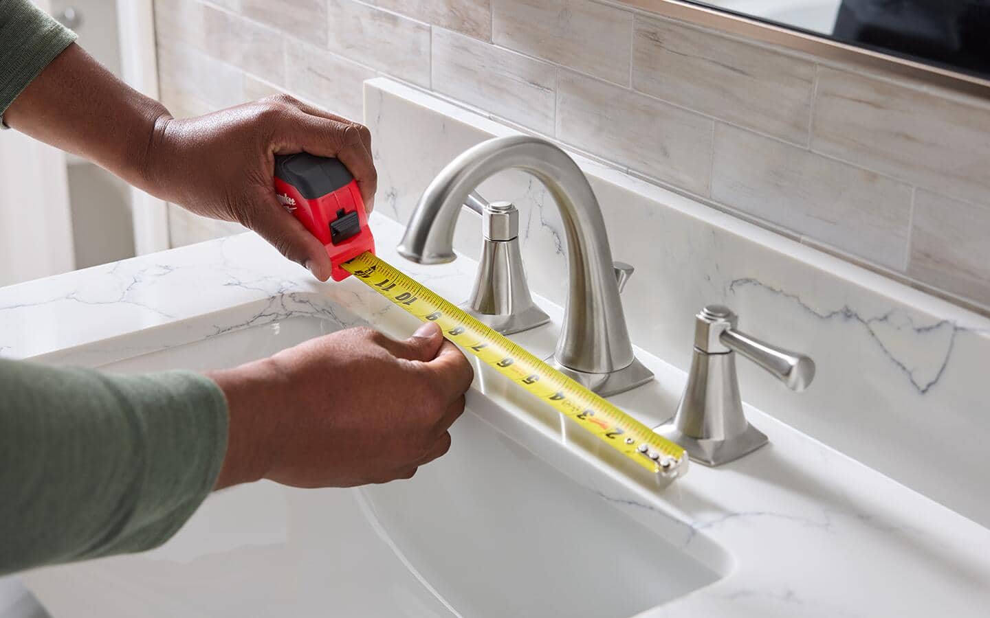 Using a tape measure to find the width of a widespread bathroom faucet.