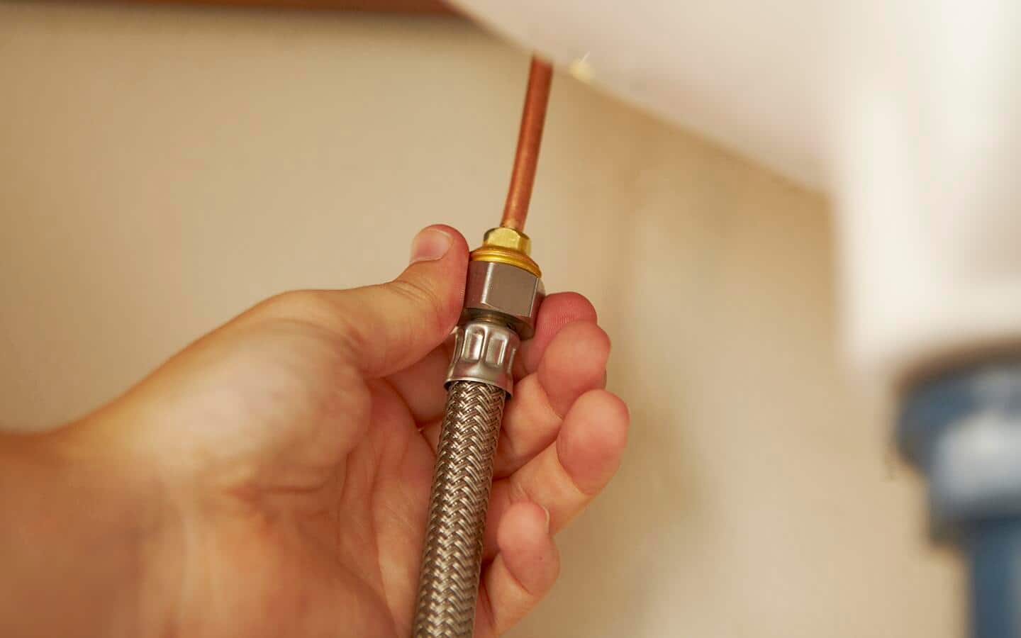 A person attaching water supply lines under a sink. A person attaching water supply lines under a sink.