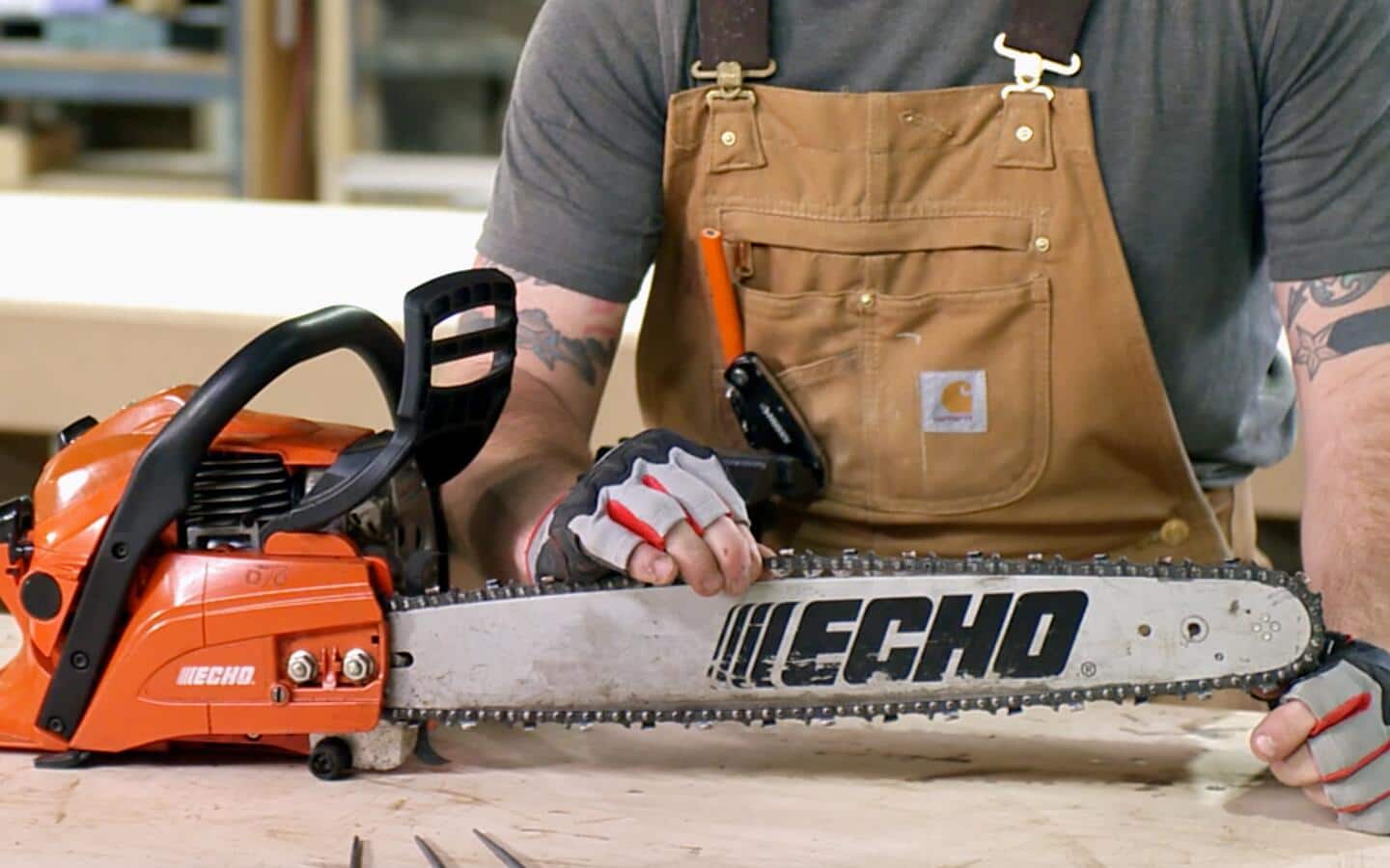 A person lifts the chain off the arm of a chainsaw lying on a workbench in a workshop. A person lifts the chain off the arm of a chainsaw lying on a workbench in a workshop.