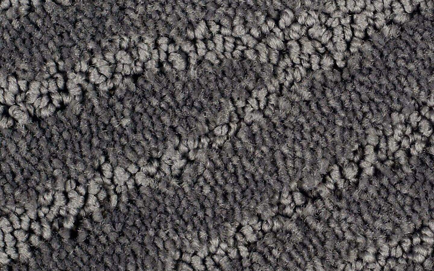 A close-up of a gray and black carpet showing a long pile.