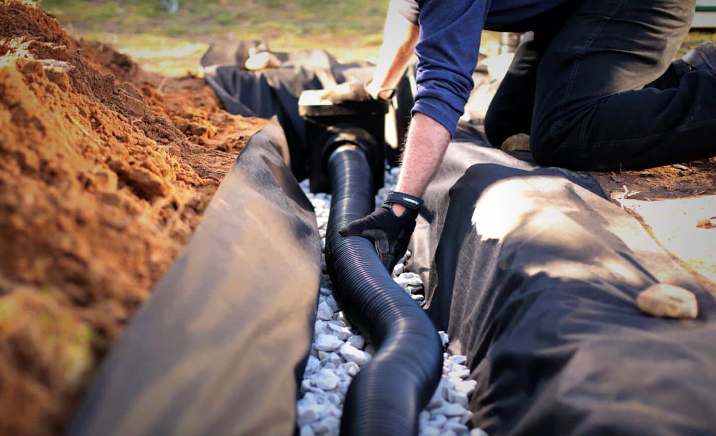 A person lays French drain pipe in a trench.