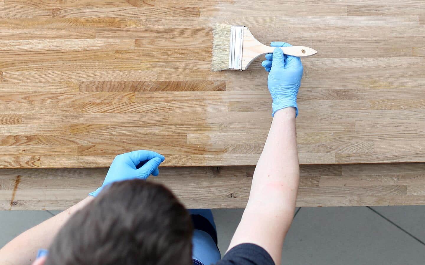 A broad paint brush being used to apply stain to a piece of wood. A broad paint brush being used to apply stain to a piece of wood.