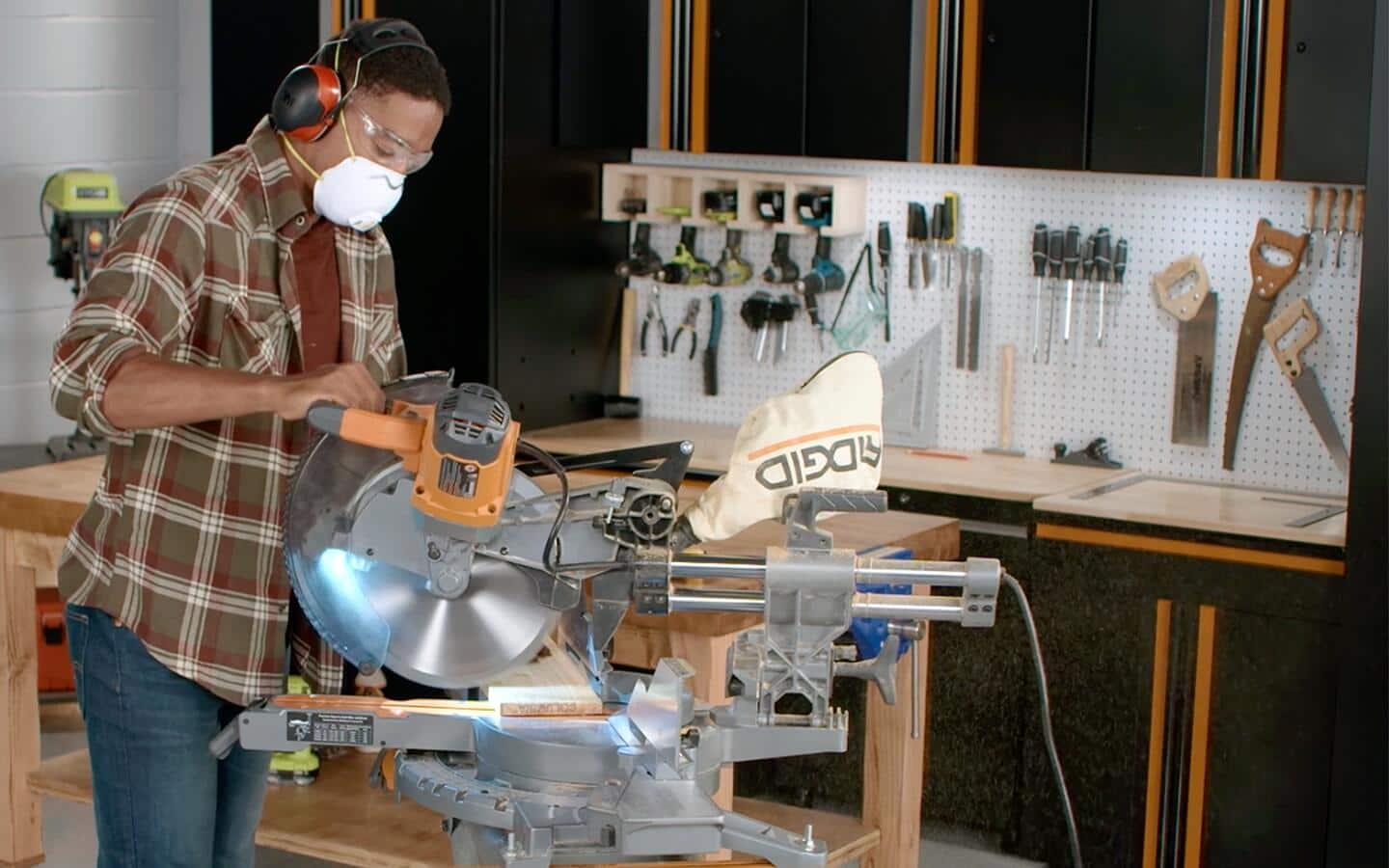 A masked person uses a miter saw to cut an angle into the end of a board.
