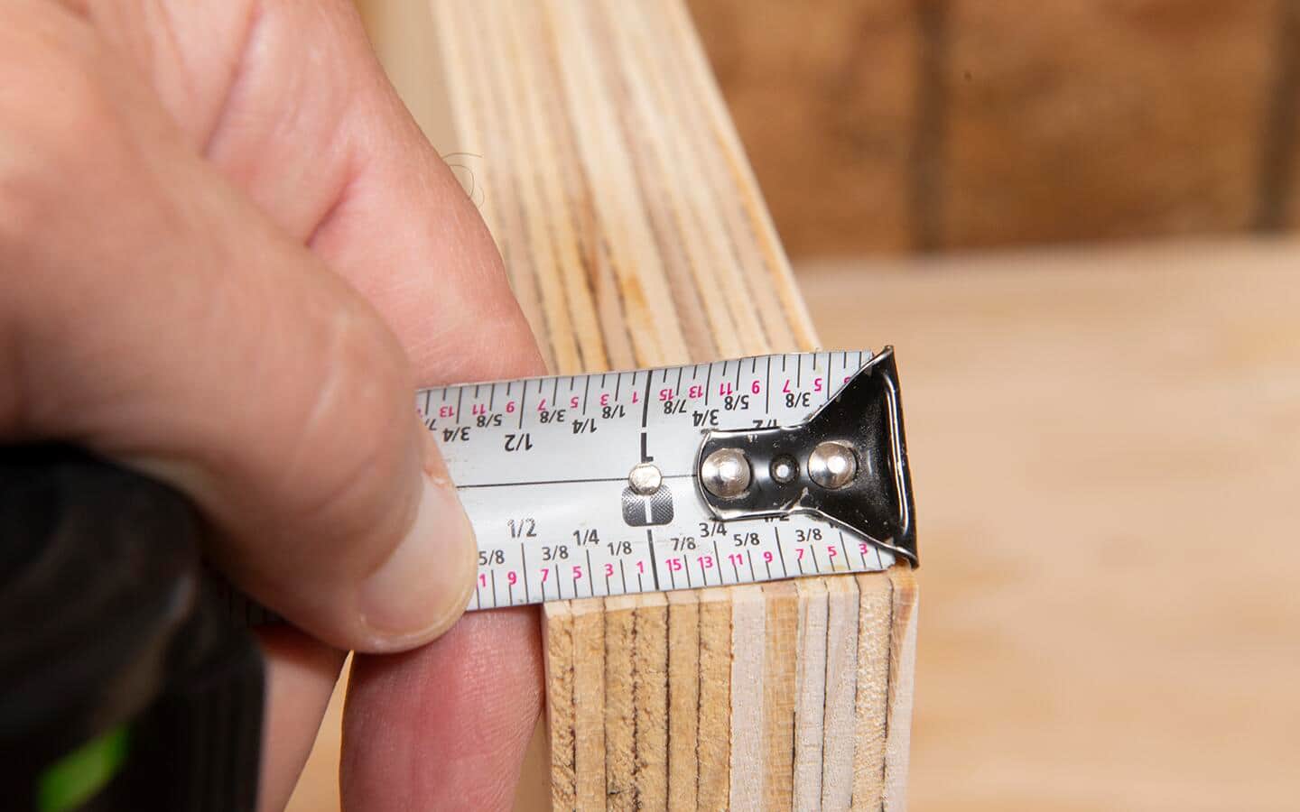 A tape measure being used to find the thickness of two pieces of plywood.