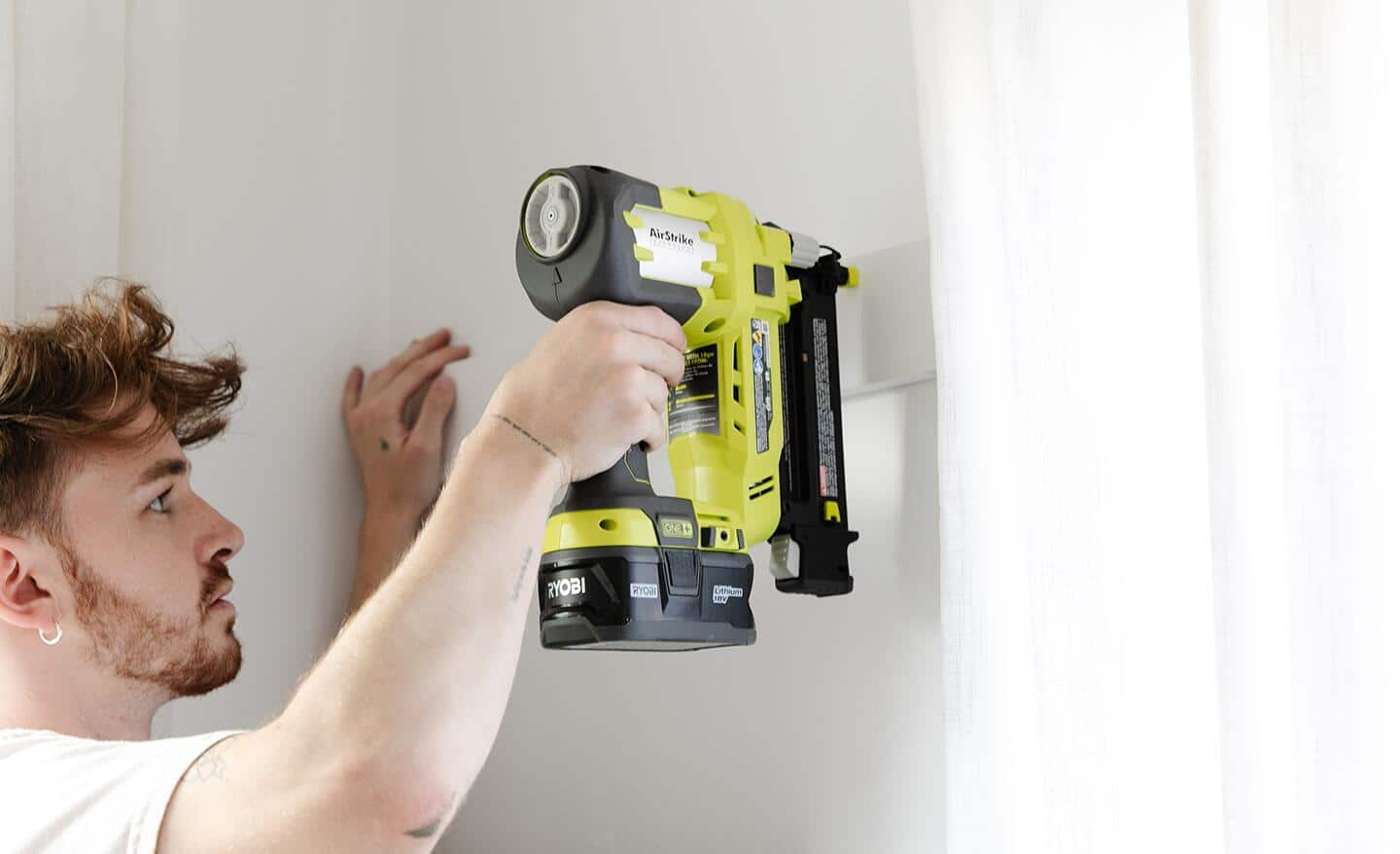 A person using a nail gun to attach boards to an accent wall.