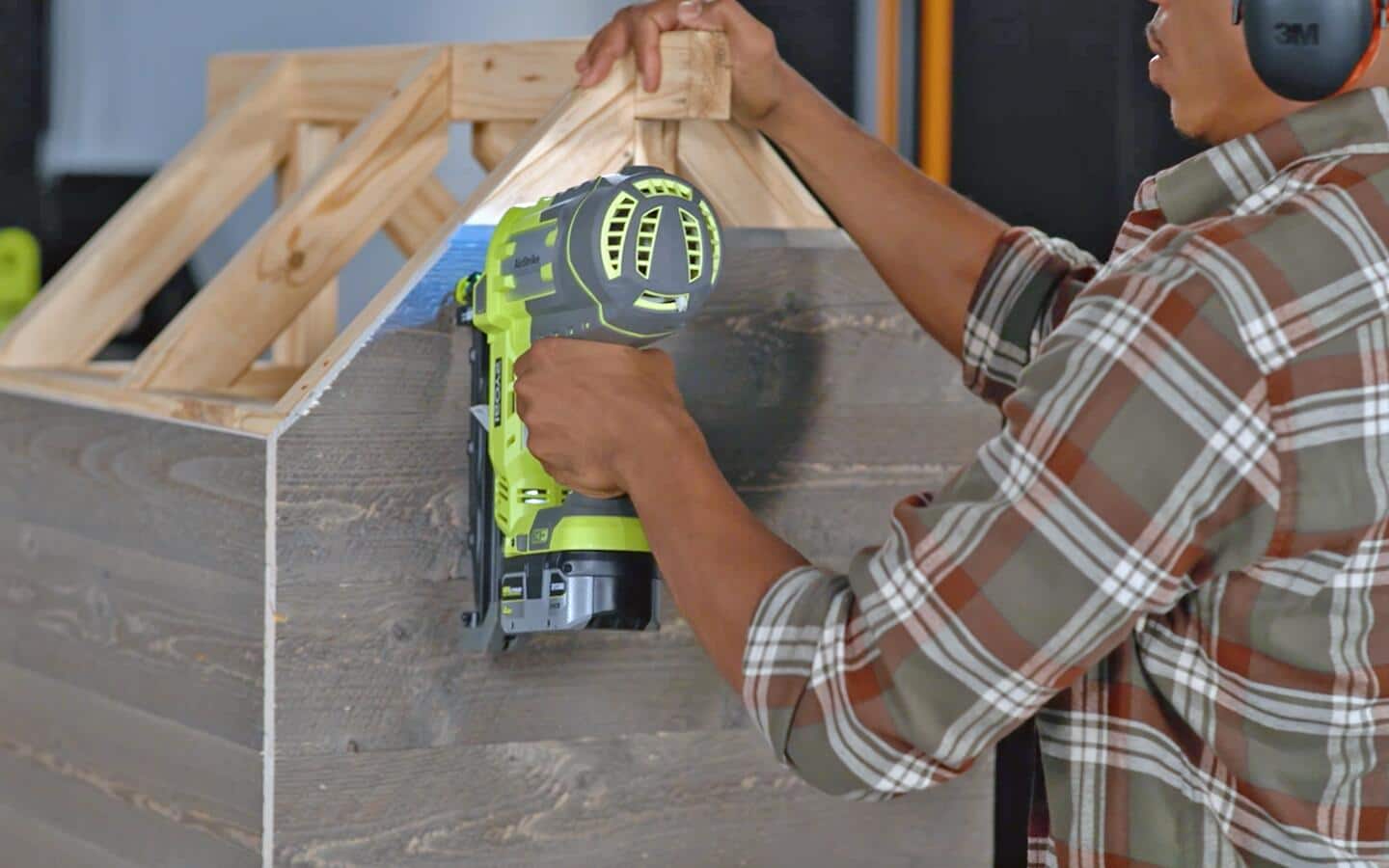 Wooden siding for the back of a dog house being installed with a nail gun.