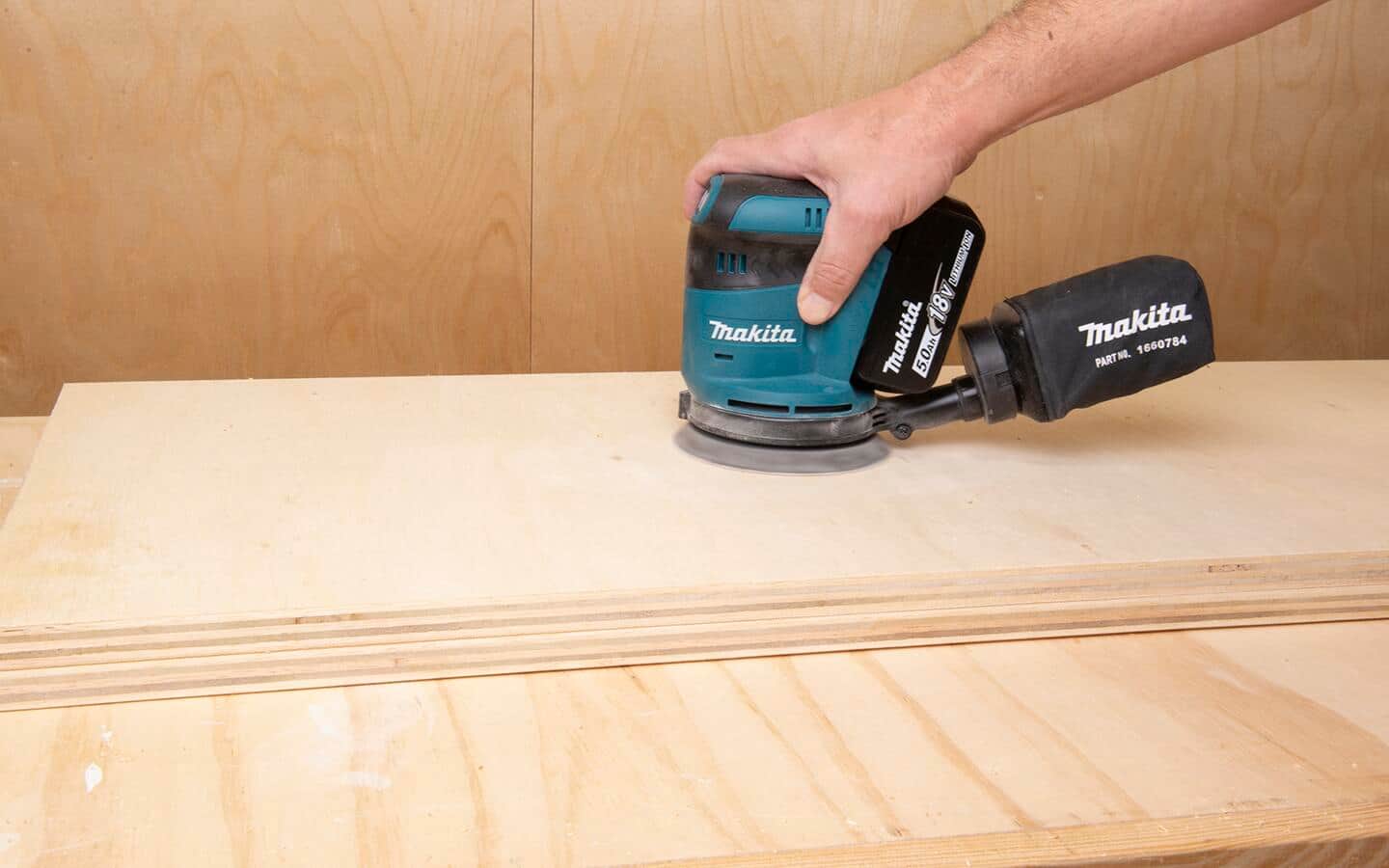 A battery powered random orbital sander is being used to sand the plywood surface of a DIY soccer rebounder board. A battery powered random orbital sander is being used to sand the plywood surface of a DIY soccer rebounder board.