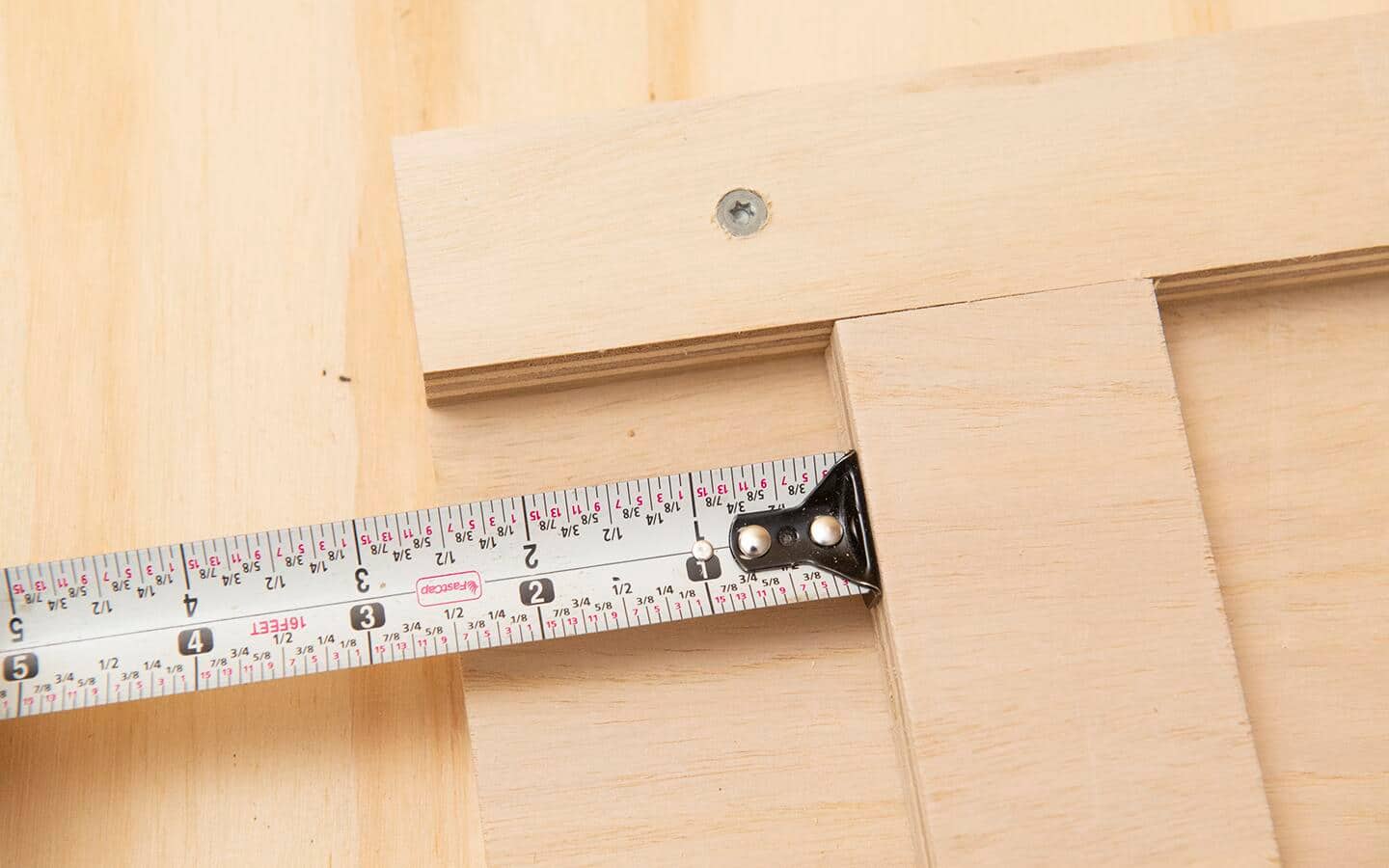 A measuring tape showing how to place the hinge board two and one half inches from the edge of the DIY soccer rebounder board. A measuring tape showing how to place the hinge board two and one half inches from the edge of the DIY soccer rebounder board.