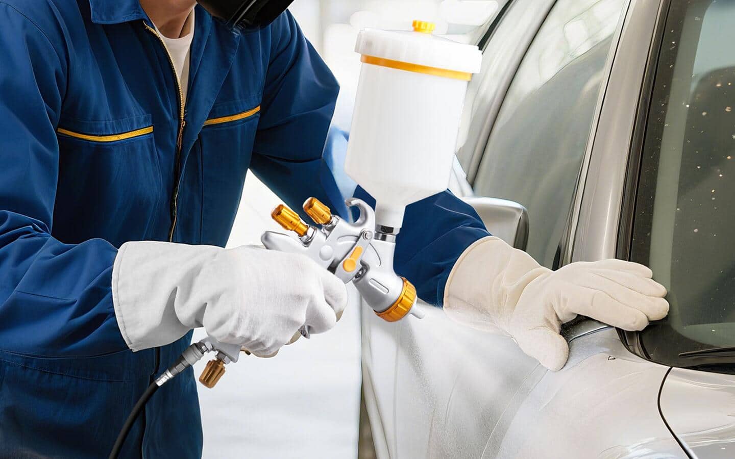 A person in white gloves uses a compressed air paint sprayer to apply white paint.
