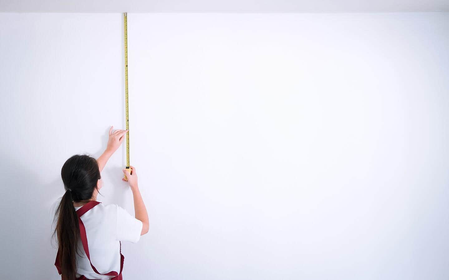 A person measures a wall vertically. A person measures a wall vertically.