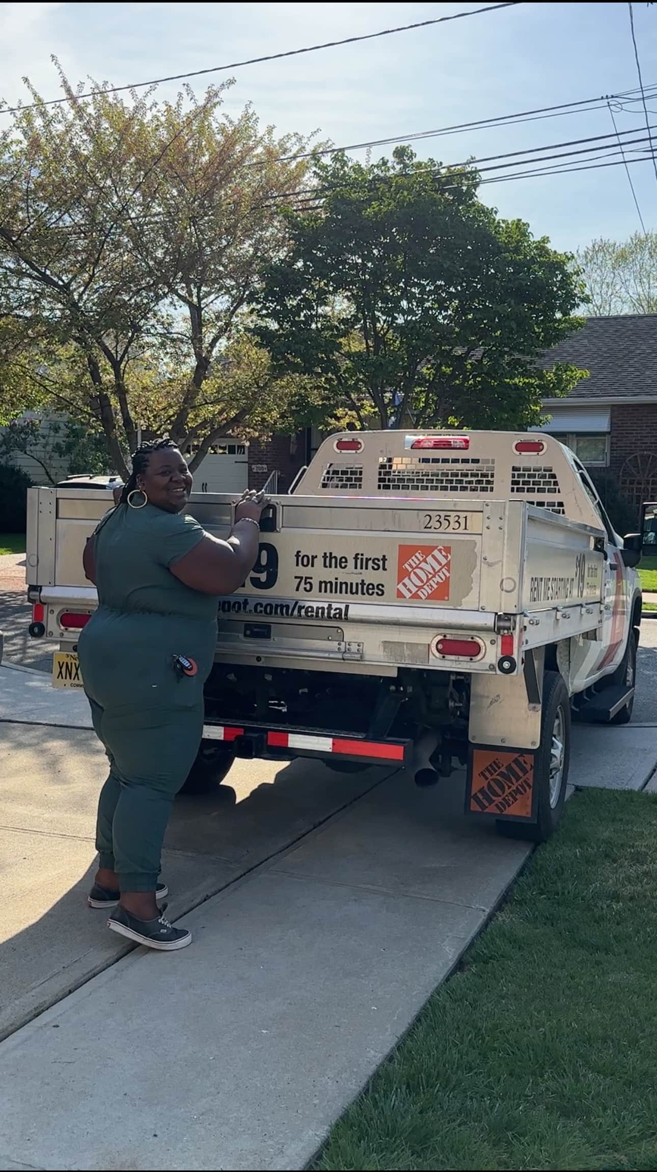 A woman standing behind a rented Home Depot flatbed truck, smiling.