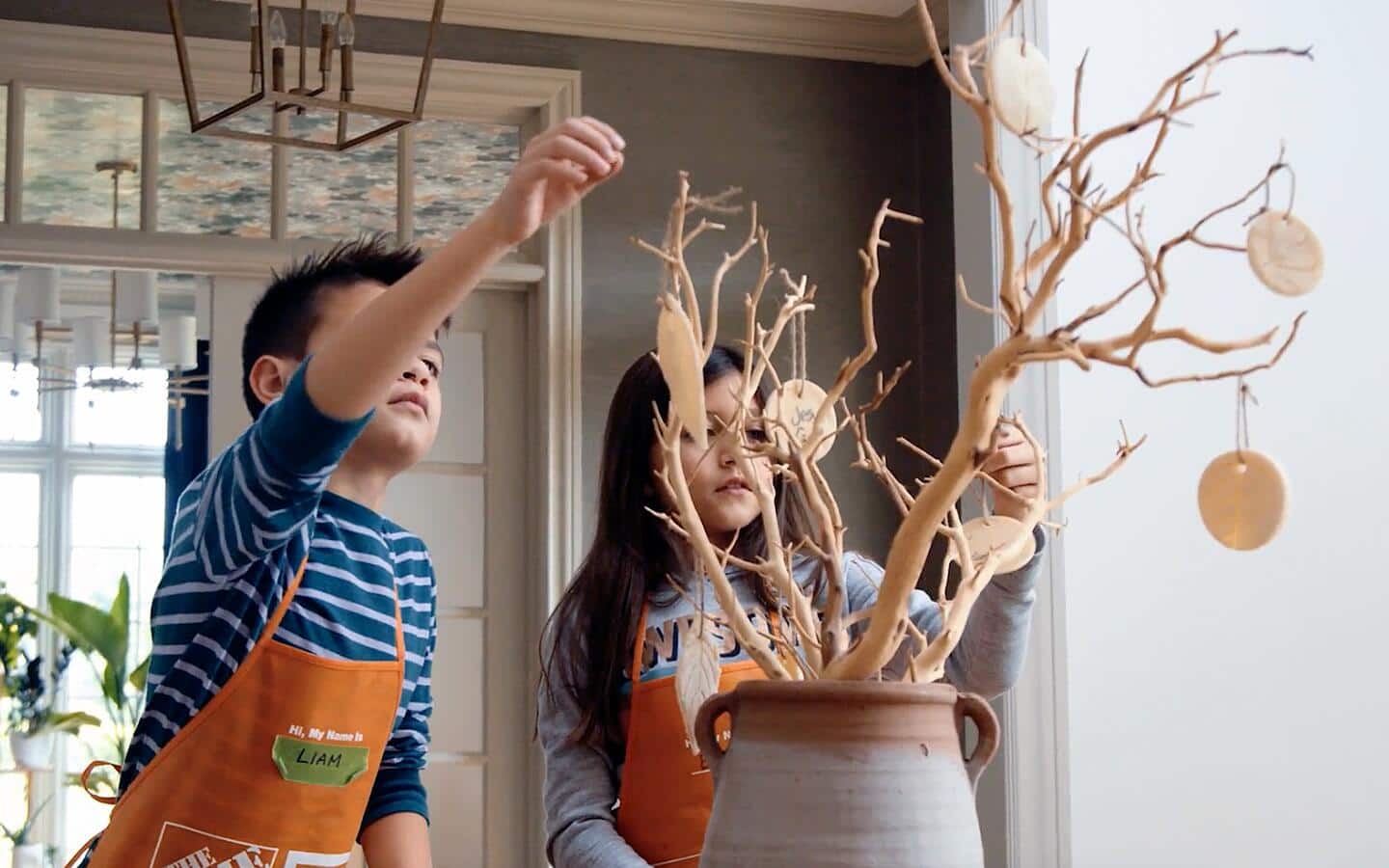 Kids hanging leaf ornaments on decorative tree branches in a vase.