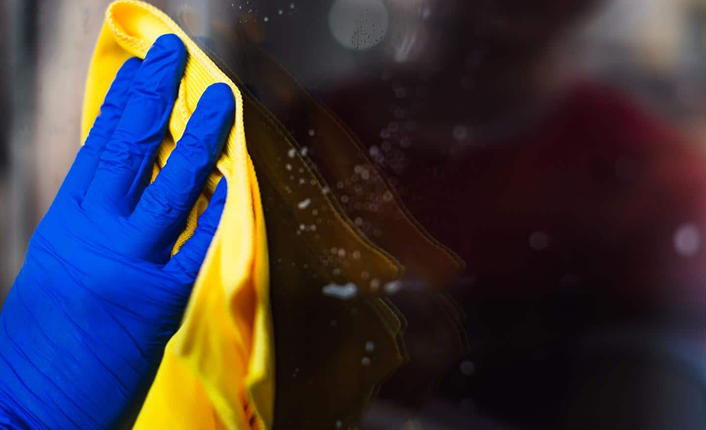 A person wearing blue gloves, cleaning glass with a yellow towel.