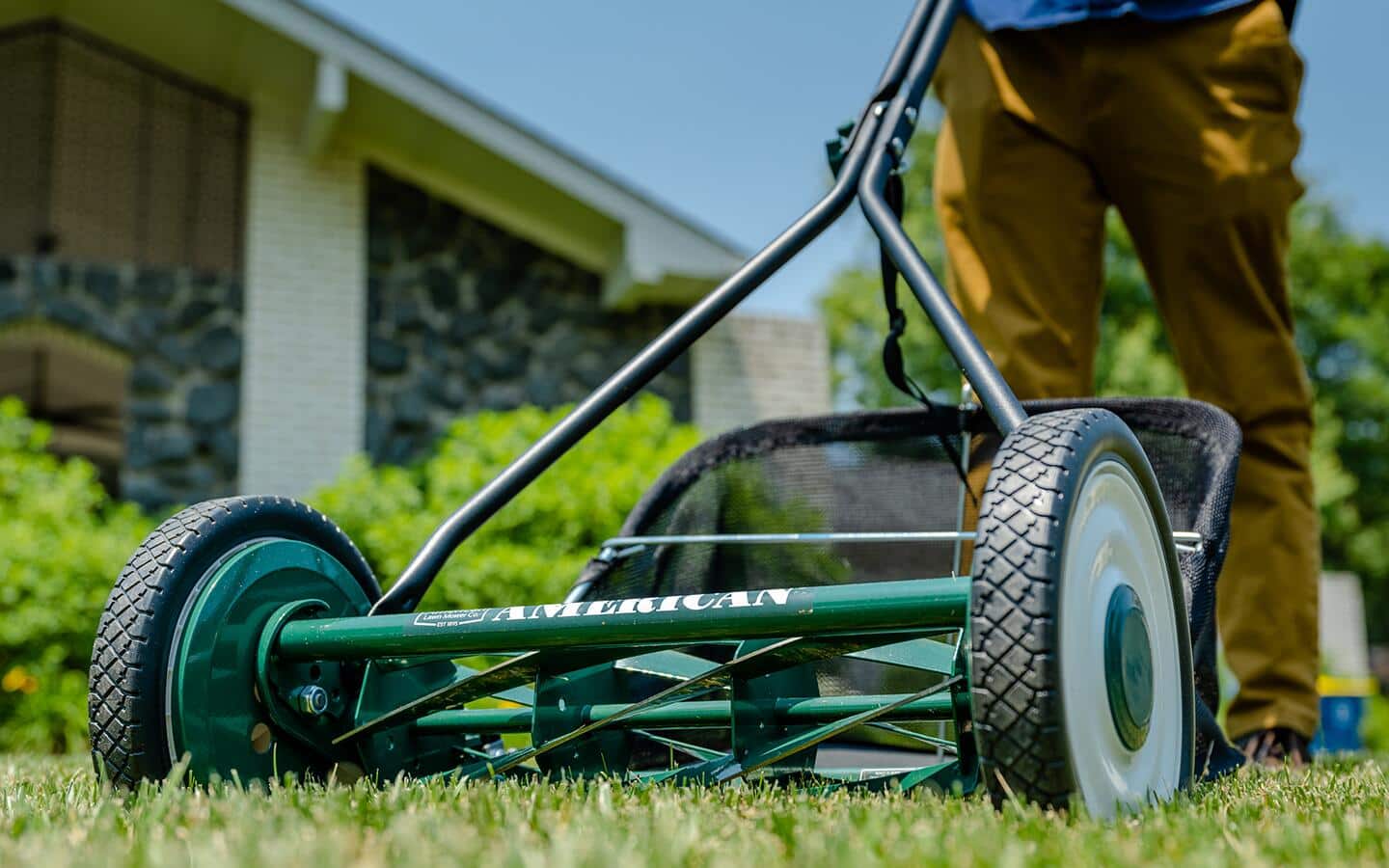 A green reel mower being used in a home's yard. A green reel mower being used in a home's yard.