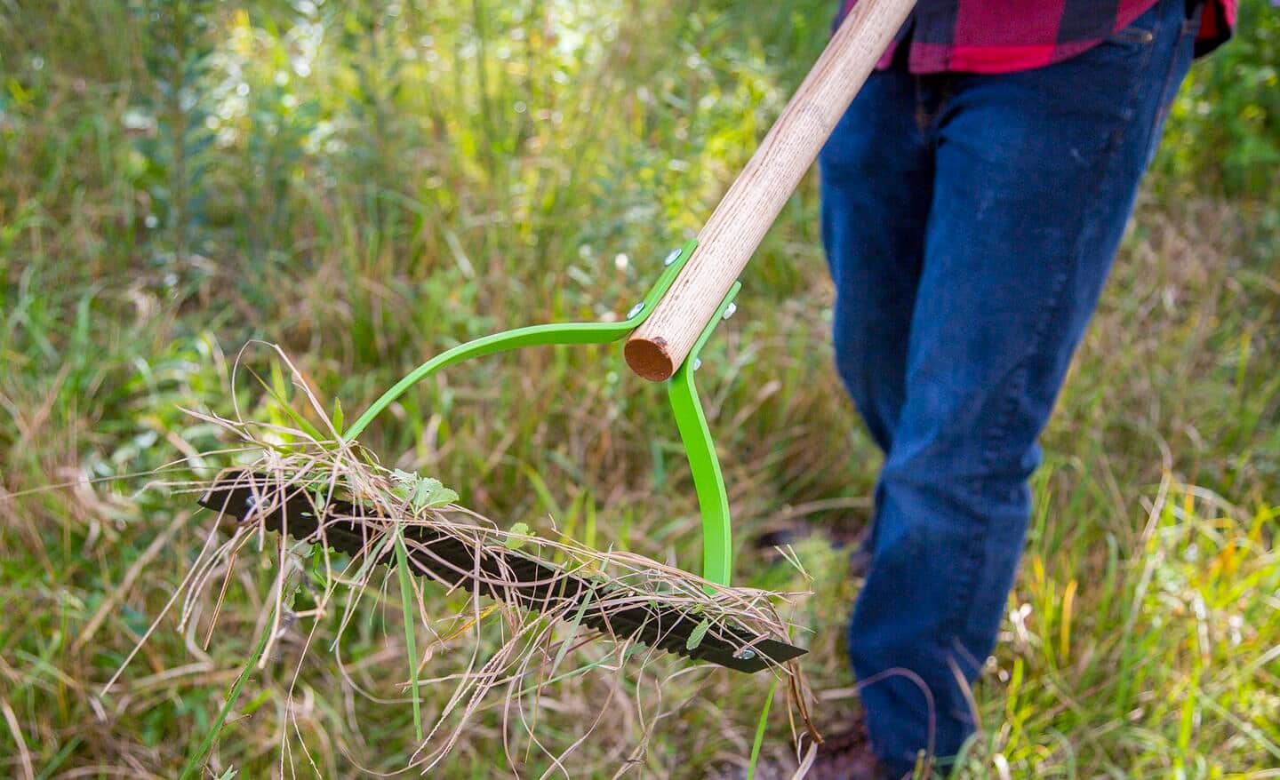 Person uses a weeding tool to clear brush