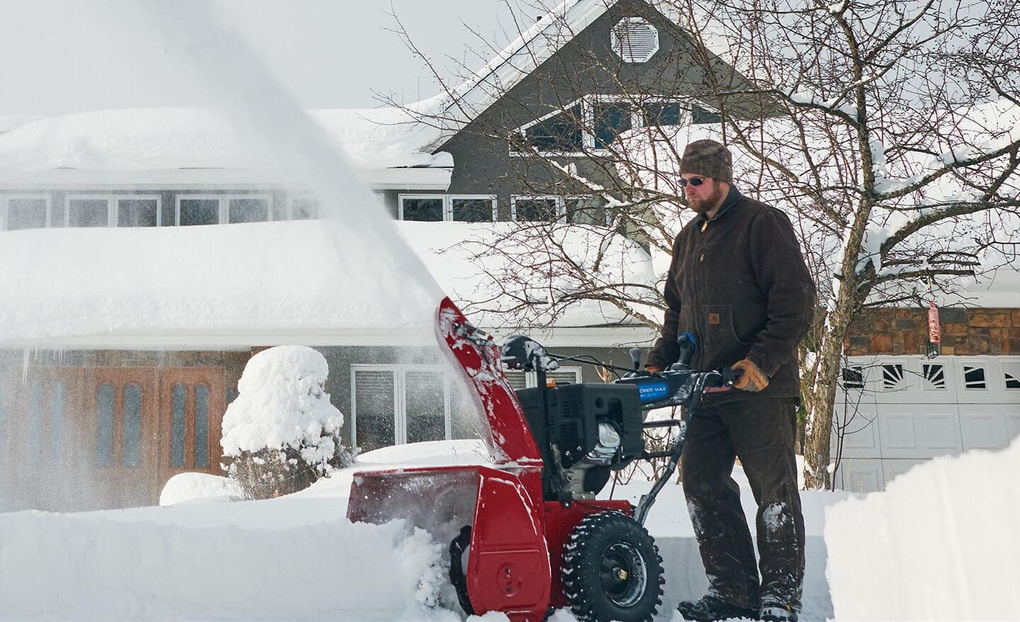 A person using a red gas snow blower to clear a driveway.