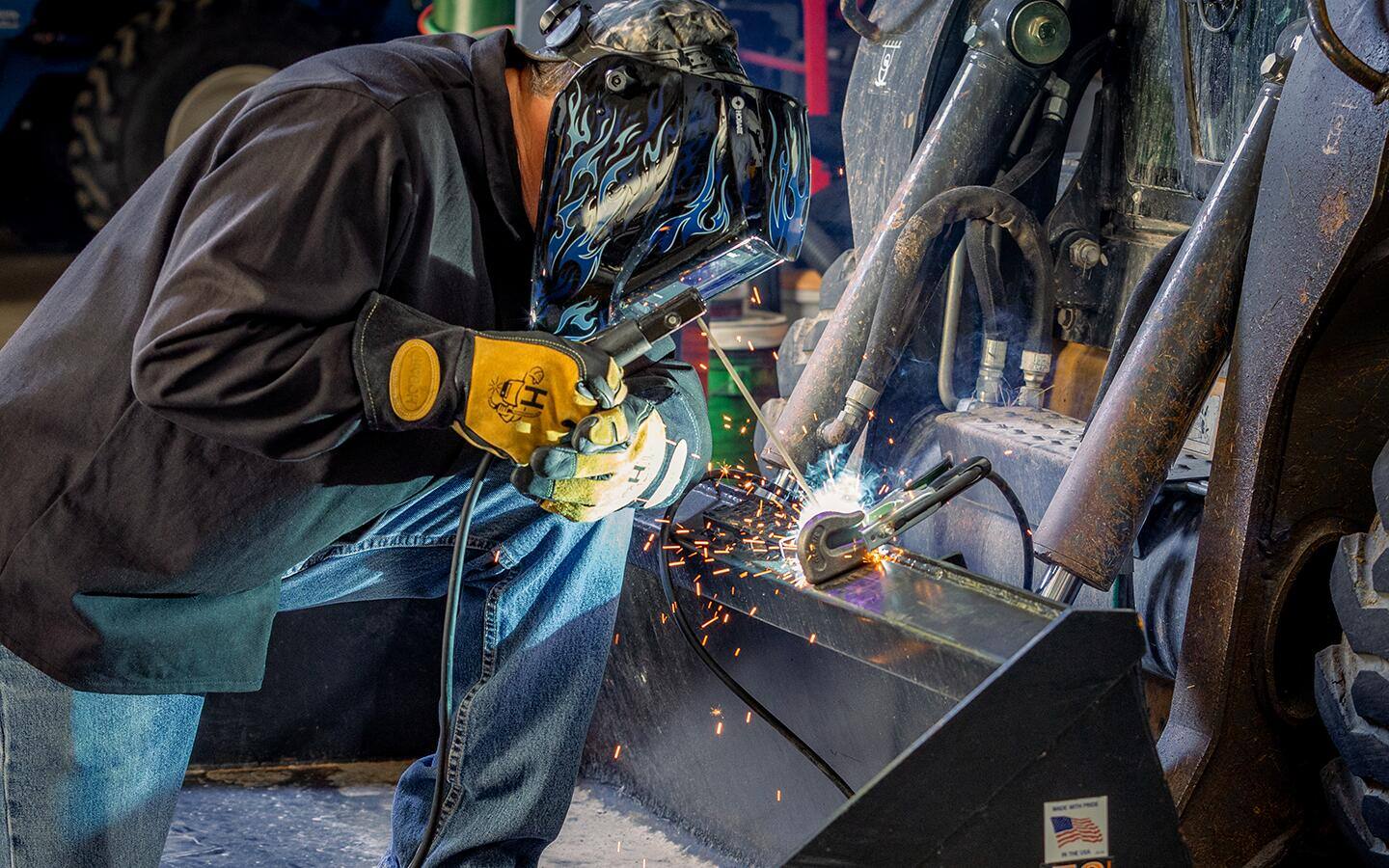A helmeted person in a black protective jacket welding metal.