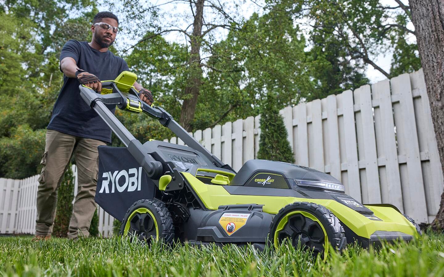 A person in safety glasses uses a light-green push mower on a healthy lawn. A person in safety glasses uses a light-green push mower on a healthy lawn.
