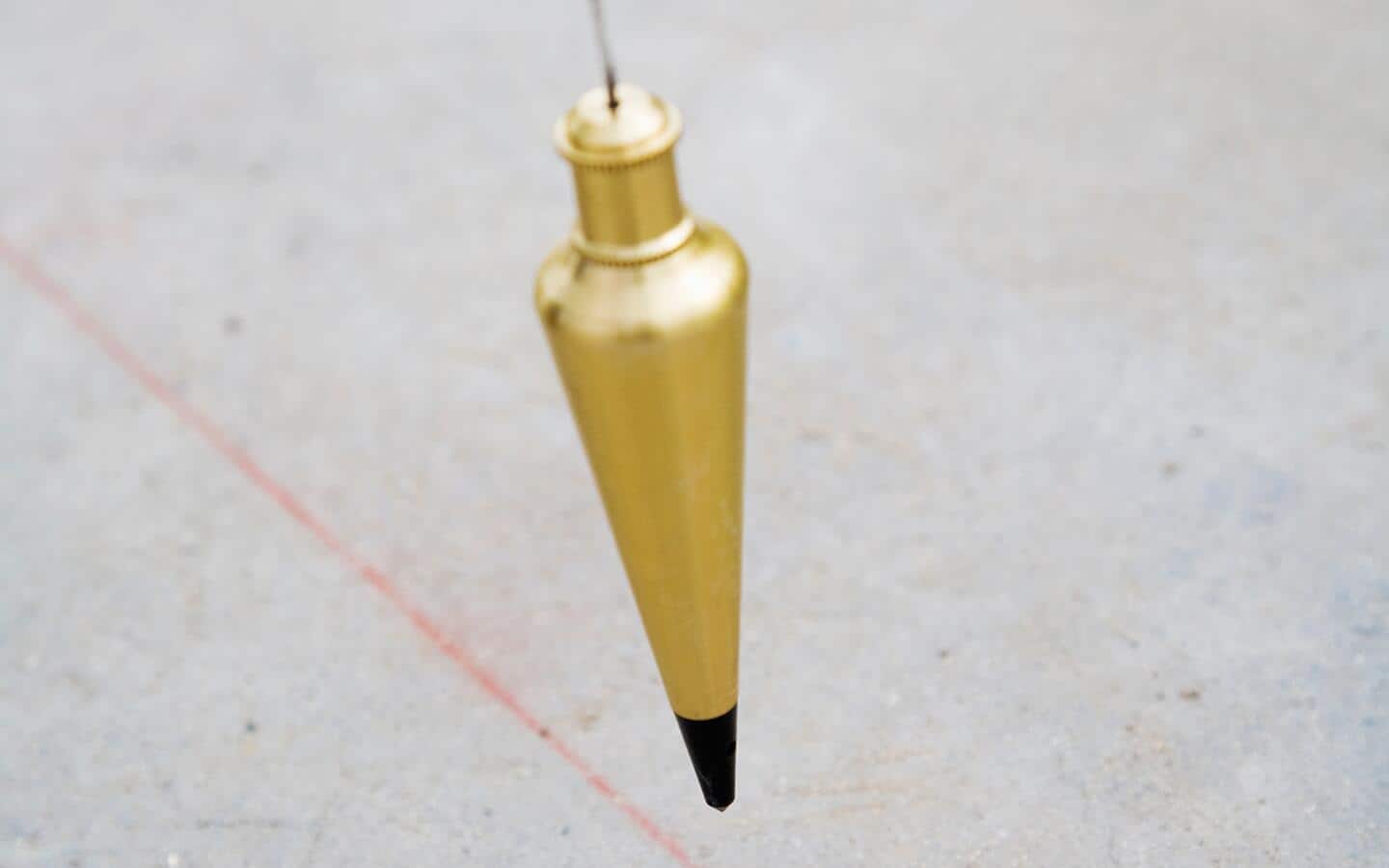 A plumb bob hangs over a snapped chalk line on a floor. A plumb bob hangs over a snapped chalk line on a floor.