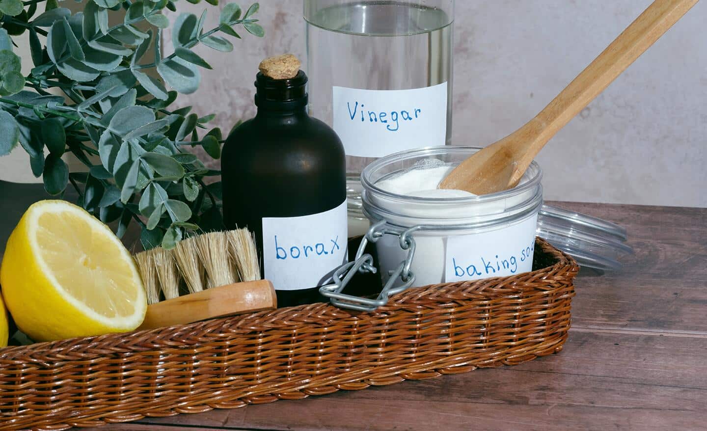 A small basket with a glass jar of borax, lemons and other natural cleaners.