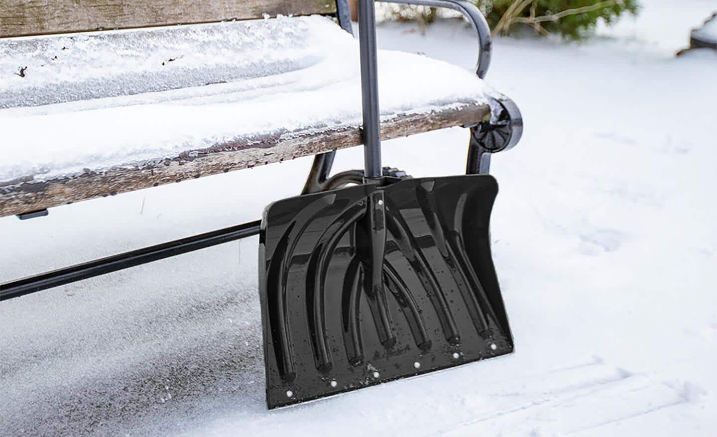 A black combination shovel leans on a bench in a snowy area. A black combination shovel leans on a bench in a snowy area.