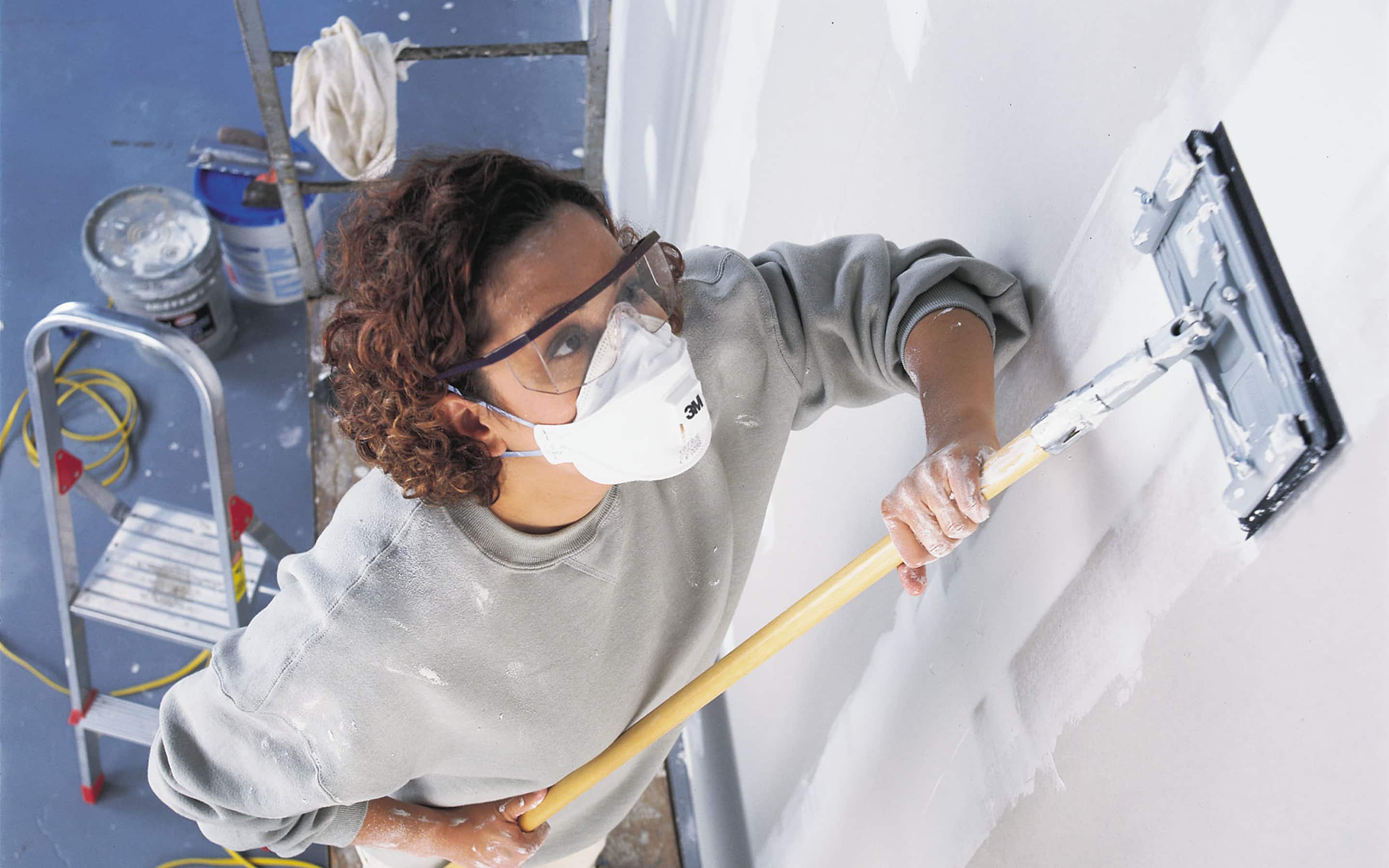 Someone sanding drywall with an extension pole.