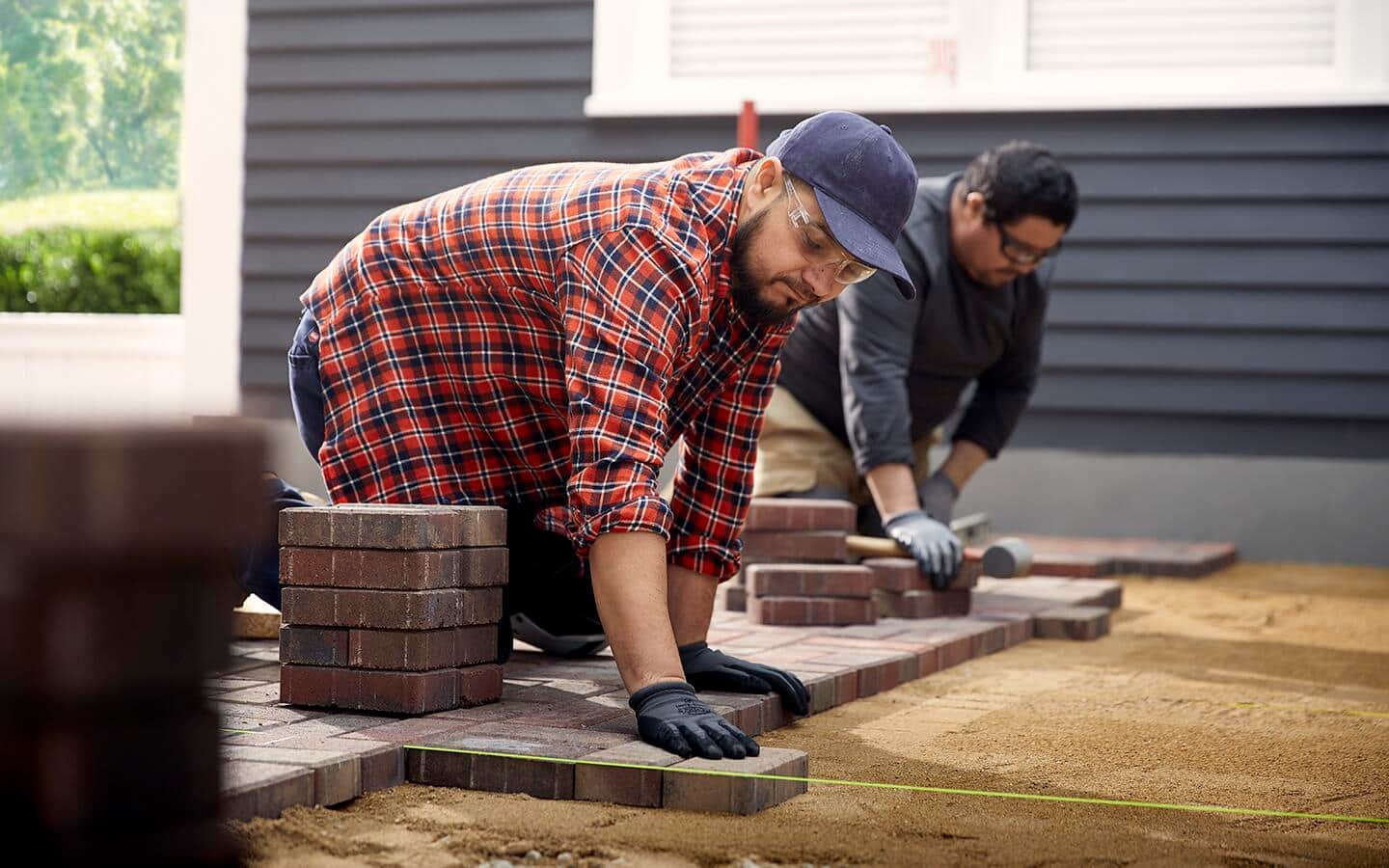 Two people install pavers in an outdoor patio space
