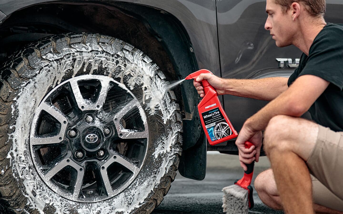 A person sprays tire cleaner onto the tire of a car.