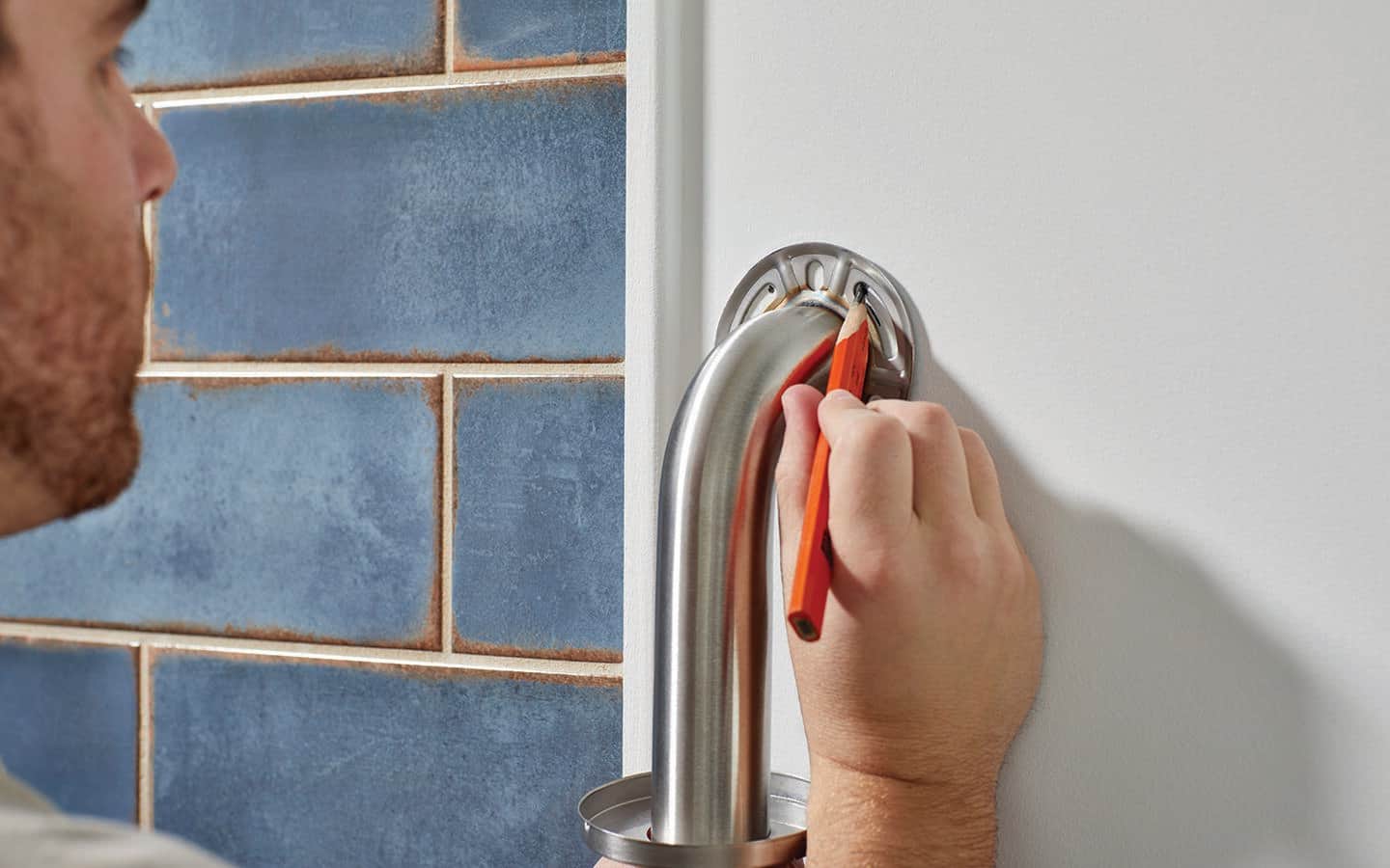 A man marks the mounting holes for the grab bar on the wall. A man marks the mounting holes for the grab bar on the wall.