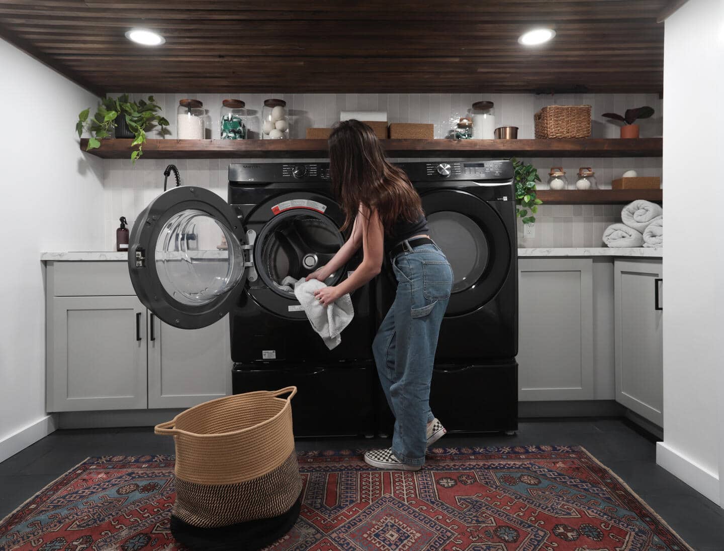 Girl loading blacker dryer with white towel in basement with large rug.