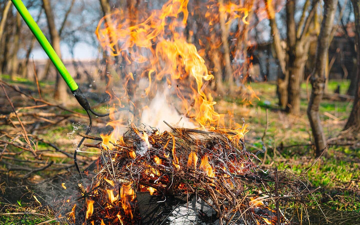 A debris fire is tended with a rake.