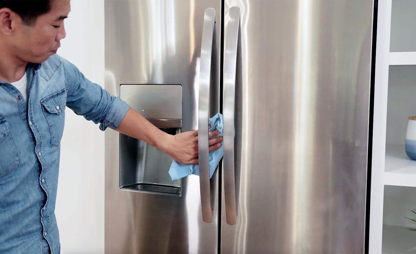 A person uses a cleaning cloth to wipe down the exterior side of a refrigerator door.